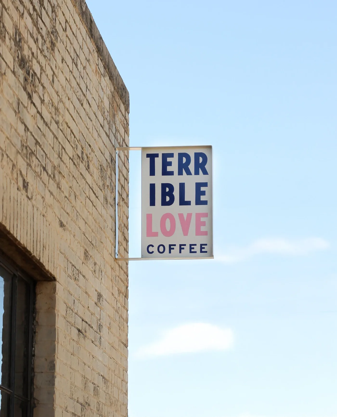 The Terrible Love Coffee sign, navy and pink on white, mounted on the brick outside